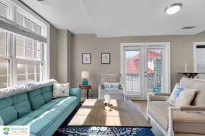 Ein Wohnzimmer mit Sofa, Sessel, Couchtisch und Blick ins Freie.