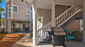 Ein zweistöckiges Haus mit einer überdachten Terrasse, einem Grill und einer Treppe.