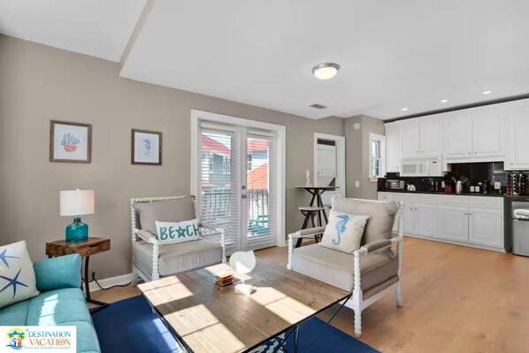 A spacious living area with a sofa, chairs, a coffee table, and a view through a sliding glass door to the outside.