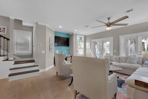 Un salon spacieux avec un escalier, un ventilateur de plafond et un grand téléviseur.