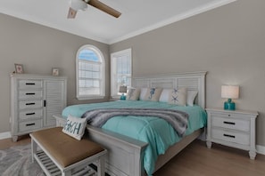 Une chambre à coucher comprenant un lit, des tables de chevet, un banc, une armoire et un ventilateur de plafond.