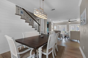 Un coin repas avec une table en bois foncé, des chaises blanches et un escalier doté d’une rampe.