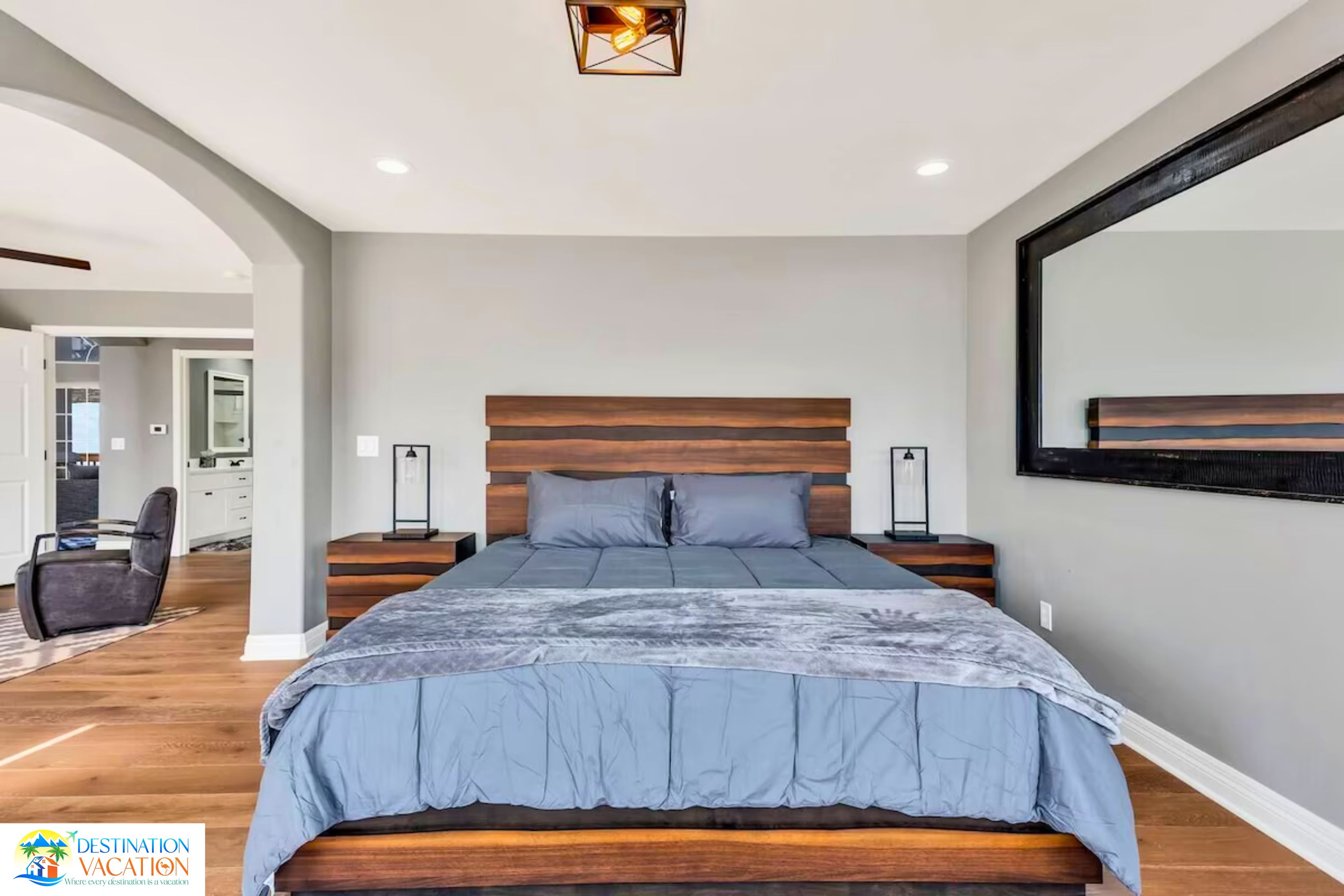 A modern bedroom with a large bed, wooden headboard, bedside lamps, and a large mirror on the wall.