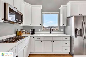 A modern kitchen with white cabinets, stainless steel appliances, and a window providing a view of a snowy landscape.