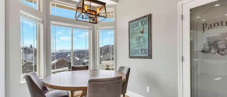 Un coin repas avec une table ronde, quatre chaises, un luminaire suspendu et une vue sur un paysage enneigé par de grandes fenêtres.