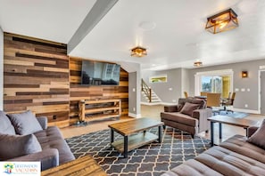 Una sala de estar moderna con una pared de madera, un televisor de pantalla plana, un sofá, una mesa de centro y una escalera que lleva a otro nivel.