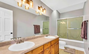 Un baño con dos lavamanos, un espejo y una ducha con puertas de vidrio esmerilado.