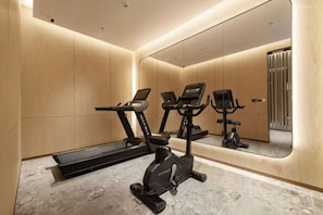 A modern gym with exercise equipment, a large mirror, and a wooden wall design. - Kusatsu Hotel (Wuxi)