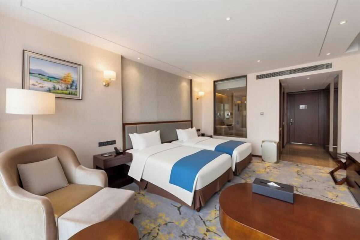 A hotel room with two beds, a sofa, a desk, a lamp, and a painting on the wall.