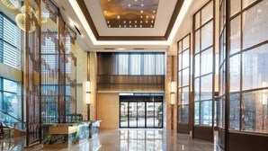 A spacious lobby with a high ceiling, large windows, and a reception desk. - REZEN HOTEL (Wuxi)