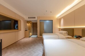 A hotel room with two beds, a large mirror, a door, and a small table with a lamp.