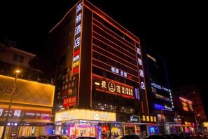 Un hotel de varios pisos con señalización iluminada, una entrada destacada y una planta baja con tiendas.