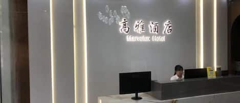 A hotel reception desk with a marble counter and a digital screen. The reception area has a modern design with vertical lighting accents.