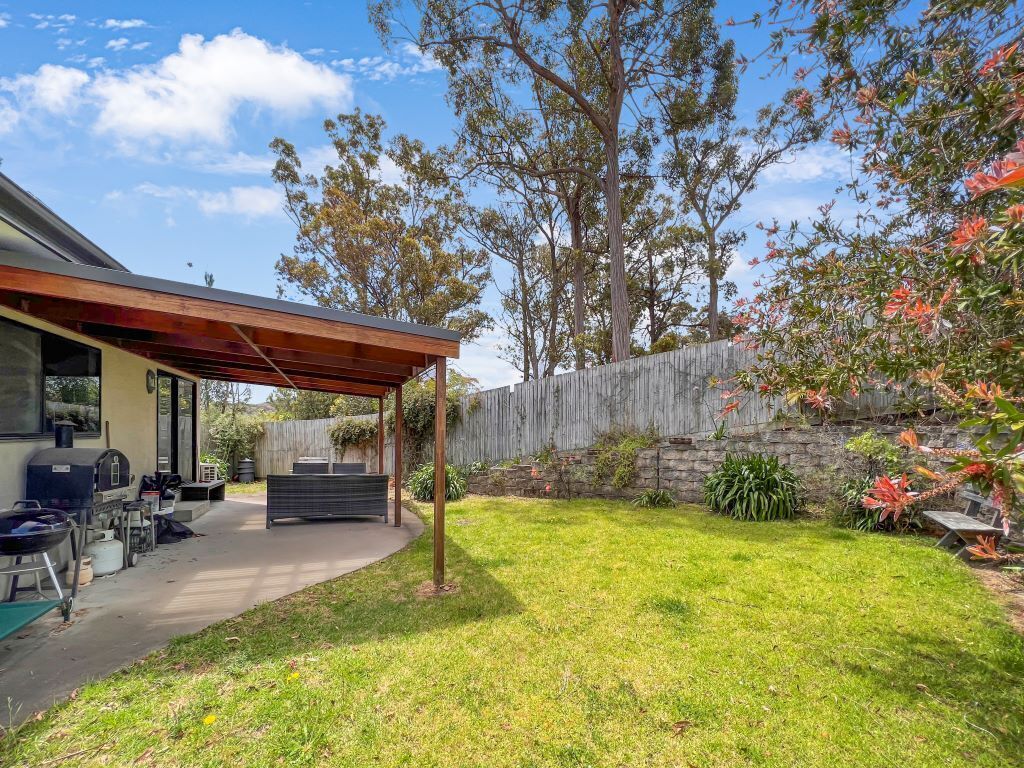 A backyard with a covered patio, a barbecue grill, and a stone wall.