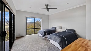 Un dormitorio con dos camas, un ventilador de techo, un ventanal y vistas al exterior.