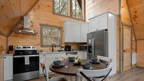 A wooden cabin kitchen with a stove, oven, refrigerator, and white cabinets. - Creekfront Views! Hot Tub/ 2 King Bed En Suites/Secluded/Arcade/Firepit/FastWifi (Pigeon Forge)