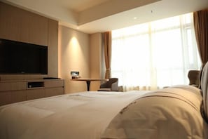 Una habitación de hotel con una cama grande, un televisor de pantalla plana, un escritorio y una silla.