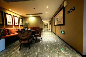 Un pasillo de hotel con una zona de recepción, un sofá, una mesa de comedor con sillas y obras de arte enmarcadas en las paredes.
