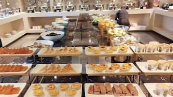 A buffet with various food items including pastries, sandwiches, and fruits.