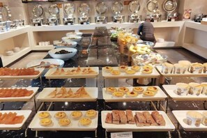 Un bufé con diferentes opciones de comida, incluyendo pasteles, sándwiches y frutas.