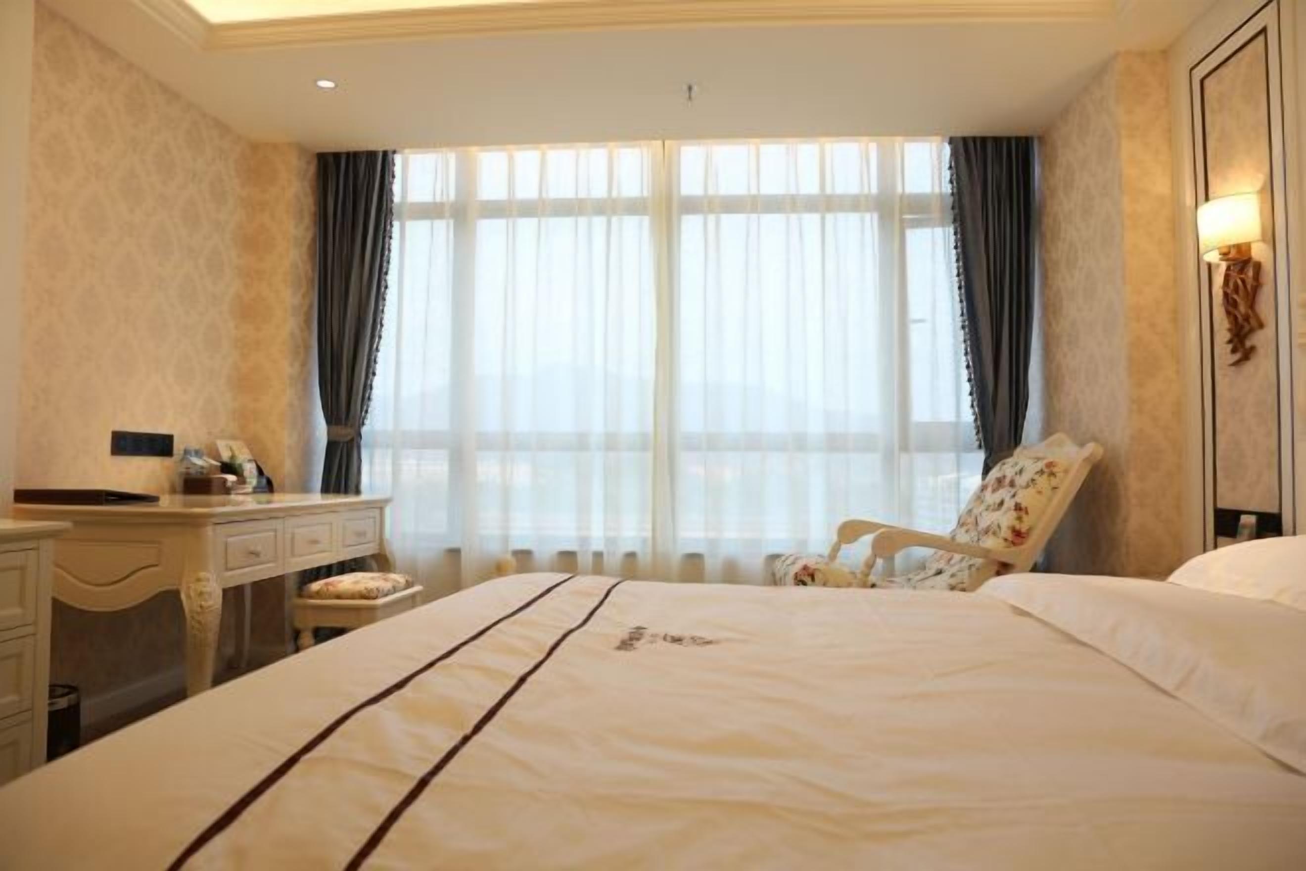 A hotel room with a large bed, a desk, a chair, and a window with curtains.