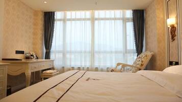 A hotel room with a large bed, a desk, a chair, and a window with curtains.