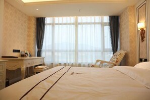 Una habitación de hotel con una cama grande, un escritorio, una silla y un ventanal con cortinas.