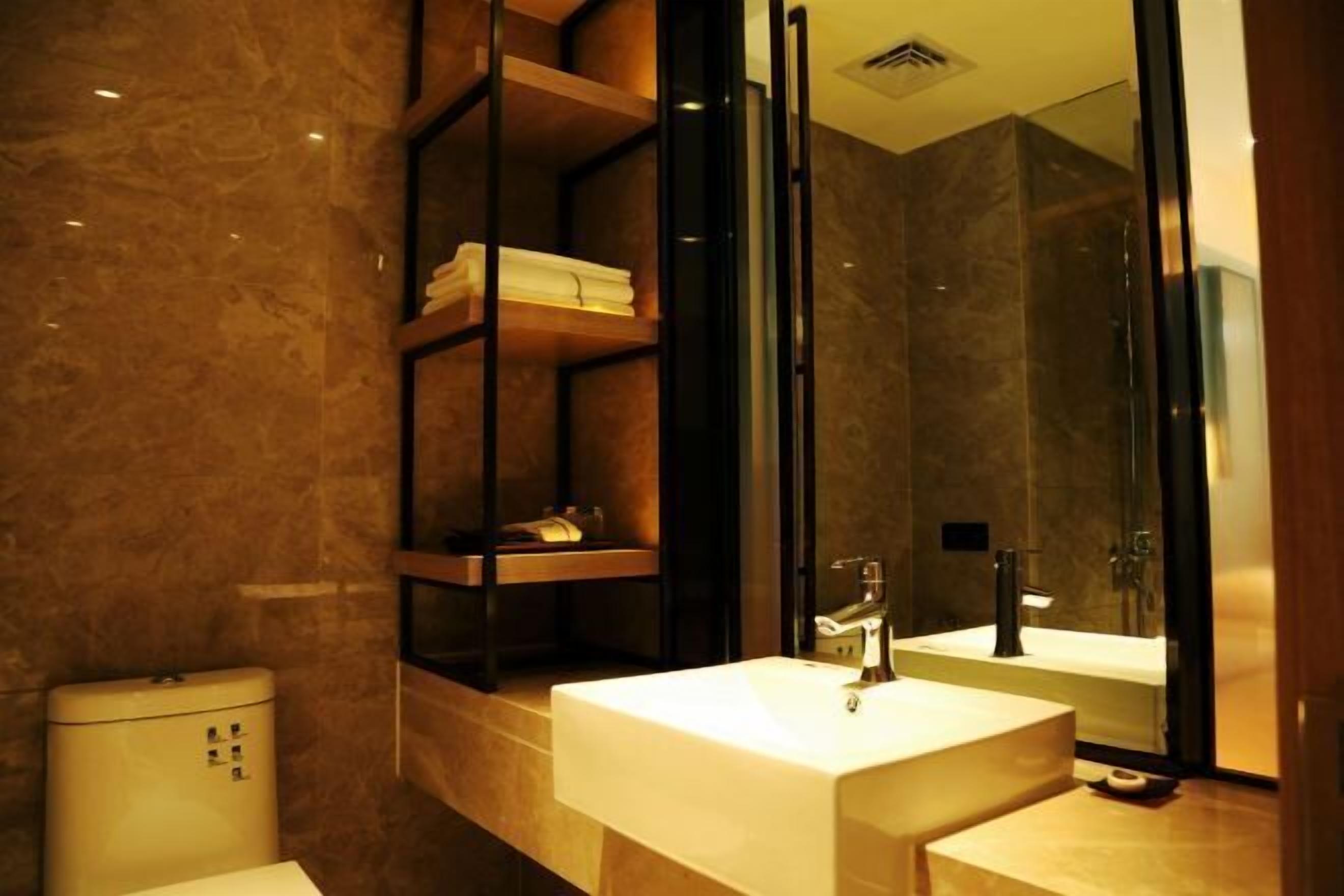 A modern bathroom with a marble floor, a white sink, a glass shower enclosure, and a built-in shelf with towels.