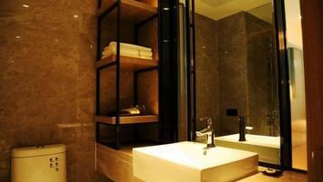 A modern bathroom with a marble floor, a white sink, a glass shower enclosure, and a built-in shelf with towels.