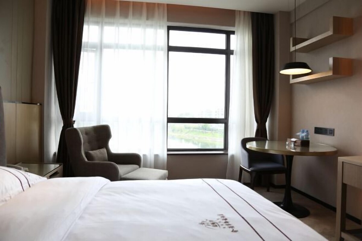 Hotellihuone, jossa on sänky, työpöytä, tuoli ja ikkuna, jossa on verhot.