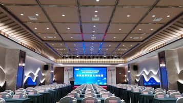 A conference room with a stage, rows of tables, and chairs.