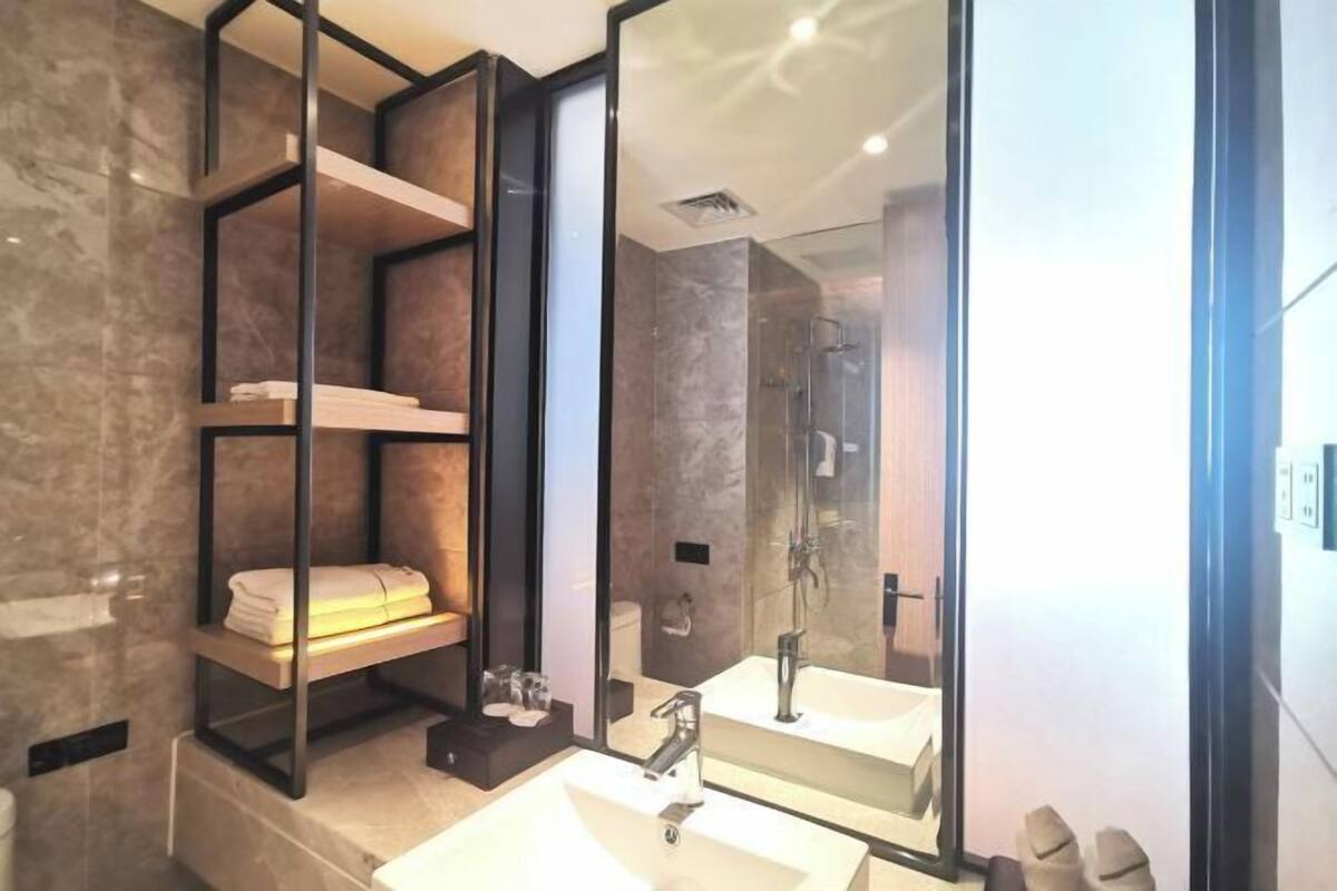 A modern bathroom with a glass-enclosed shower, a large mirror, and built-in shelves with towels.