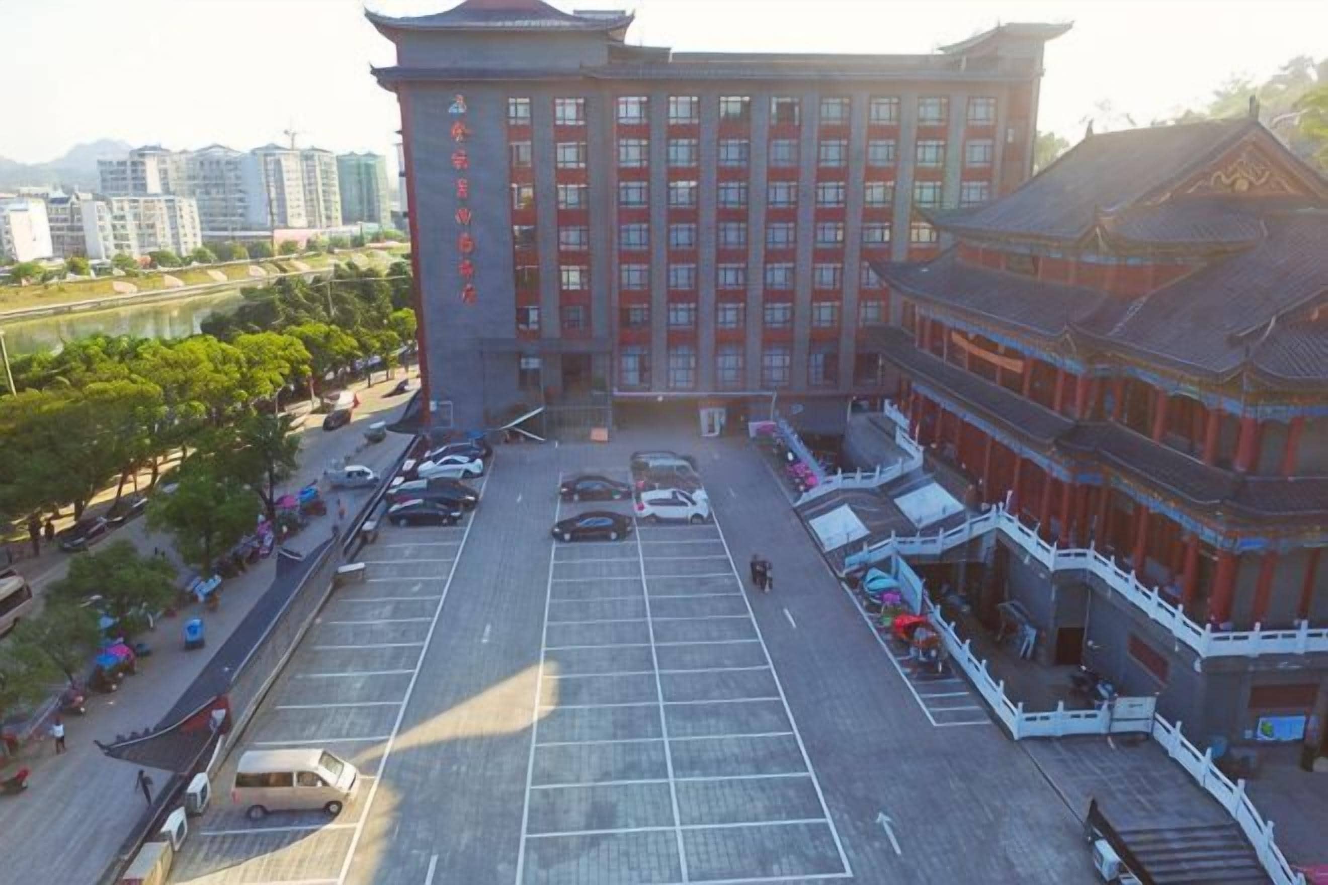A multi-story hotel with a traditional architectural style, a parking lot, and a river in the background.