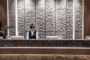 A reception desk with a textured wall behind it, a plant to the left, and a dark wooden counter in the foreground. - Yongfu County Golden Coast Royal Blessing Hotel (Yongfu)