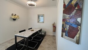 Un comedor con una mesa de mármol, sillas negras, una lámpara en el techo, un jarrón con flores y un cuadro abstracto de colores en la pared.