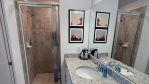 Un baño moderno con ducha acristalada, un lavamanos espacioso con espejo y obras de arte enmarcadas en la pared.