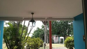 Un espace extérieur abrité, doté d’un luminaire suspendu, entouré d’une végétation luxuriante et avec un bâtiment en arrière-plan.