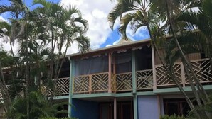 Un bâtiment à deux étages doté d’un balcon, entouré de palmiers et de verdure.