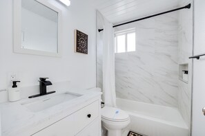 Een moderne badkamer met een witte marmeren wastafel, een zwarte kraan, een toilet en een douche.