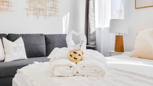 A neatly made bed with rolled towels and a cup of coffee, a grey sofa with a pillow labeled "HOPE", and a lamp on a bedside table. - Milpitas Central Private 3Bd Home~ Convenience! (Milpitas)