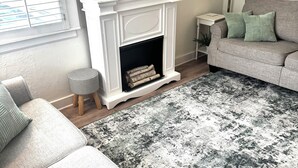 A living room with a fireplace, a sofa, a rug, and a side table. - Cozy Neutral Farmhouse Welcomes Peaceful Retreat (Muskegon)
