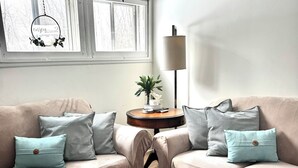 A living room with two beige sofas, patterned cushions, a small side table with a plant, and a patterned rug. - Cozy Neutral Farmhouse Welcomes Peaceful Retreat (Muskegon)