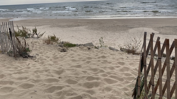 A sandy beach with a wooden fence and sparse vegetation. - Cozy Neutral Farmhouse Welcomes Peaceful Retreat (Muskegon)