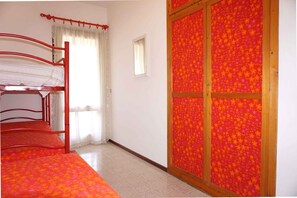 Ein Zimmer mit Etagenbett, kleinem Fenster und einer Tür mit blumigem Wandpapier.