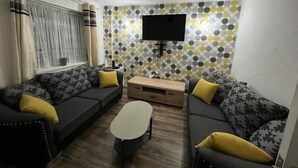 A living room with two sofas, a coffee table, and a TV on the wall. - House Sleeps 6 with Private Garden (Birmingham)