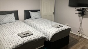 A bedroom with two beds, a television mounted on the wall, and a door. - House Sleeps 6 with Private Garden (Birmingham)