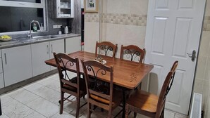 A dining area with a wooden table and chairs, a kitchen with a sink and cabinets, and a white door. - House Sleeps 6 with Private Garden (Birmingham)