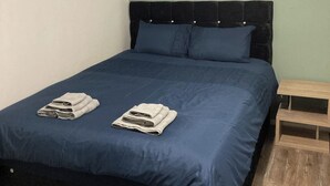 A neatly made bed with a dark blue bedspread and two folded towels on the bed. - House Sleeps 6 with Private Garden (Birmingham)