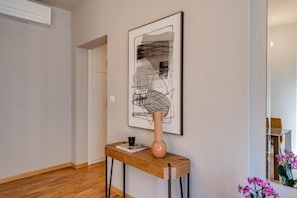 A hallway with a wooden console table, a vase, and a framed abstract painting.