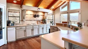 Een moderne keuken met witte kasten, een houten plafond en grote ramen met uitzicht op de omgeving.